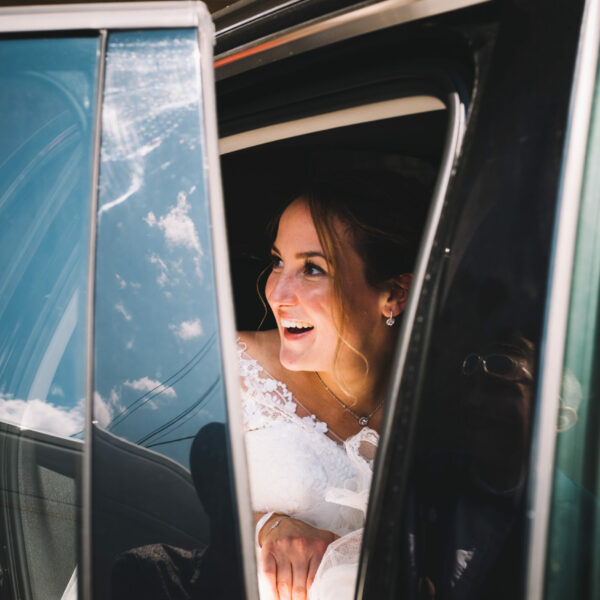 Une mariée qui rit dans une voiture avec la portière ouverte