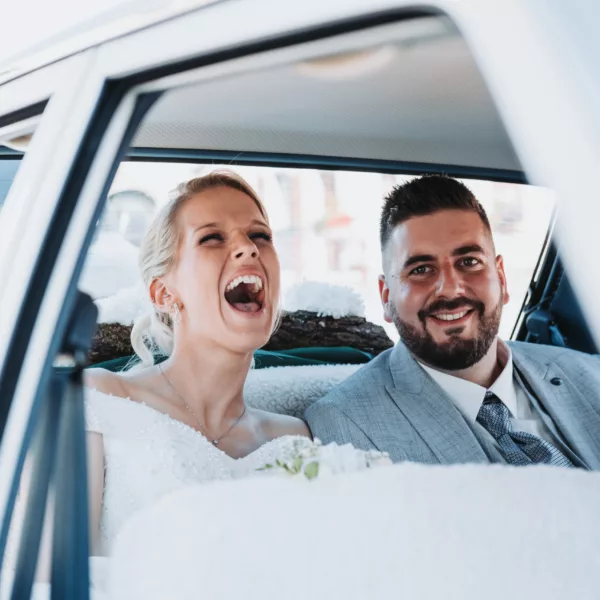 Un couple de mariés dans une voiture avec la mariée qui rit aux éclats, en Haute-Saône