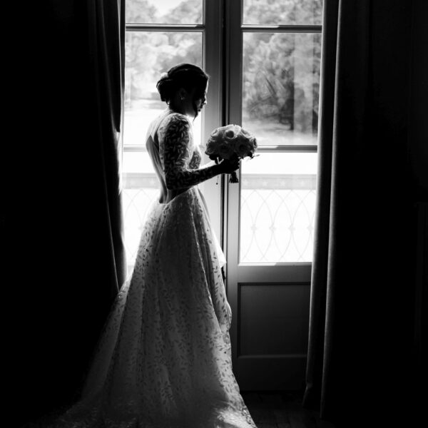 Une mariée pensive avec un bouquet de fleurs devant une fenêtre au château de Quincey en Bourgogne