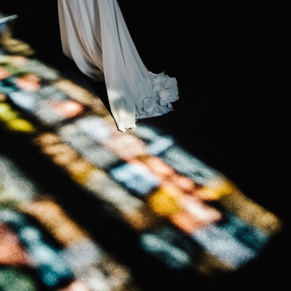 Une robe de mariée éclairée par la lumière des vitraux d'une église, dans le Doubs.