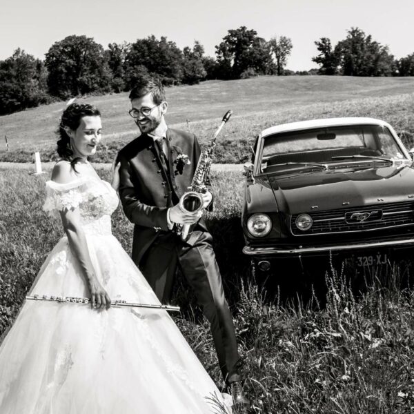 Un couple de mariés musiciens qui posent avec leurs instruments de musique devant une Ford Mustang, dans le Doubs en Franche-Comté.